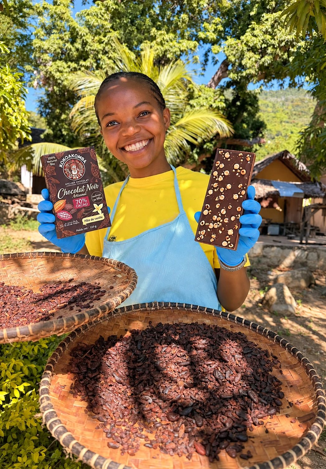 Une chocolatière souriante présente une tablette KokoaKomba Chocolat noir 70 % à la pâte de vanille, devant des vans de fèves de cacao